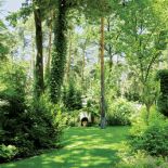 W oddali widać kamienną ziemiankę. Ogród z leśną ziemianką