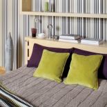 Zielone i fioletowe poduchy oraz tapeta w paski ożywiają sypialnię.