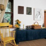 Żółty fotel i niska szafka w ciemnym morskim kolorze.