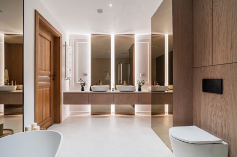 Duży salon kąpielowy z podwójną strefą umywalkową i imponującymi lustrami. Szlachetne materiały wykończeniowe i ciepłe, nastrojowe oświetlenie.