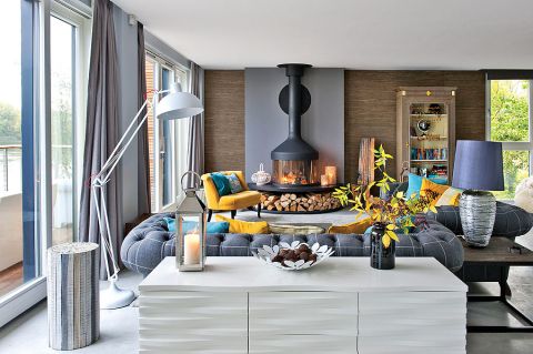 W salonie oprócz kominka, dominują szarości przełamane żółtymi dodatkami i mięsistymi tkaninami.