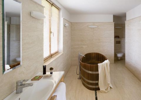 Ascetyczna łazienka wyłożona jest trawertynem. Po środku stoi drewniana wanna przypominająca cebrzyk.