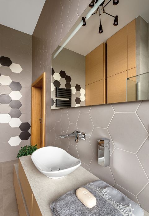 W ŁAZIENCE DZIECI POŁĄCZONO SZARE PŁYTKI O HEKSAGONALNYCH KSZTAŁTACH Z PROSTYMI PANELAMI Z NATURALNEGO DREWNA.