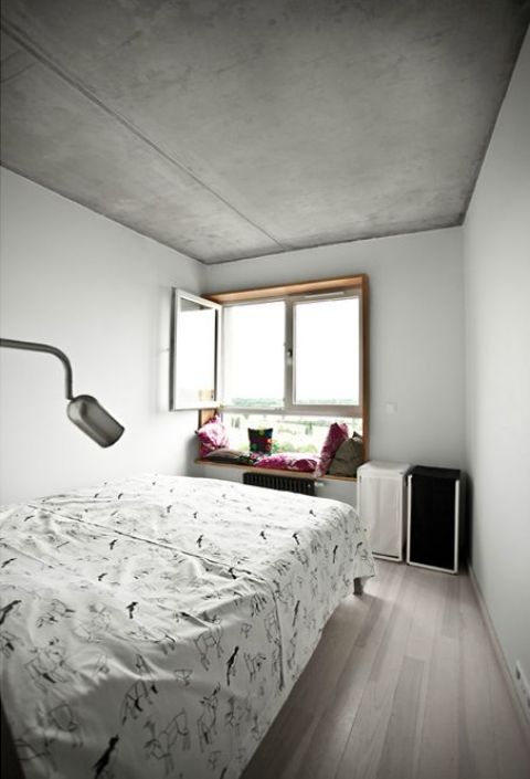 Sypialnia w jasnych kolorach. Na parapecie kolorowe poduszki.