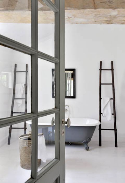 W minimalistycznej łazience mocnym akcentem jest wanna pomalowana na szaro i bambusowe wieszaki-drabiny.