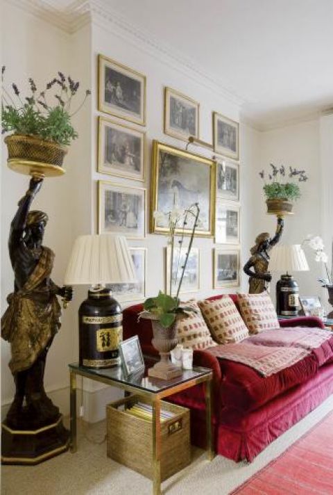 Czerwone obszycia na kanapie, jasne poduszki i kolekcja obrazów na ścianie.