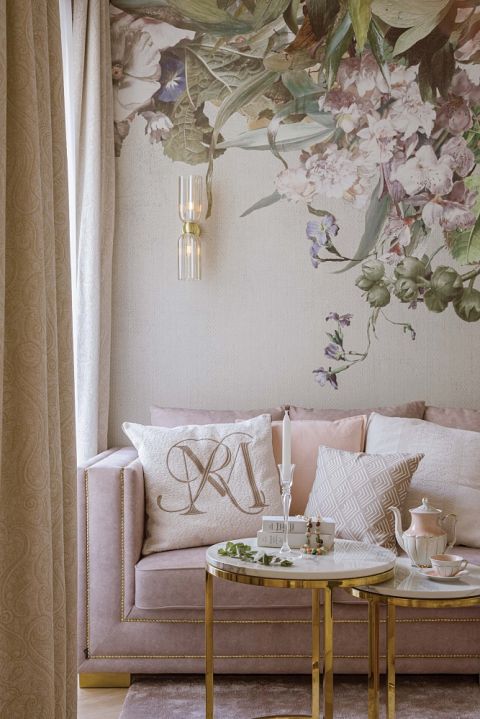 różowa sofa na tle tapety w kwiaty w salonie