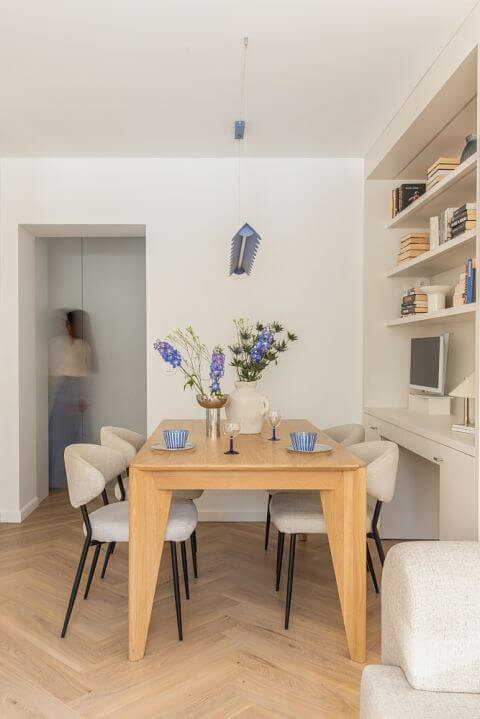 Drewniany stół, beżowe krzesła i niebieska lampa nad stołem w jadalni w mieszkaniu 60 m2 w bloku