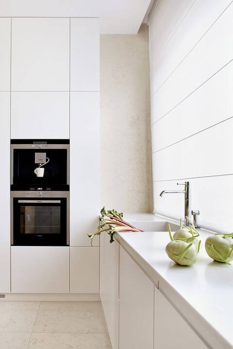 Na podłodze leży wapień perlino bianco. Matowe szafki zestawiono z wyspą-stołem z szarzonego dębu. Sprzęt