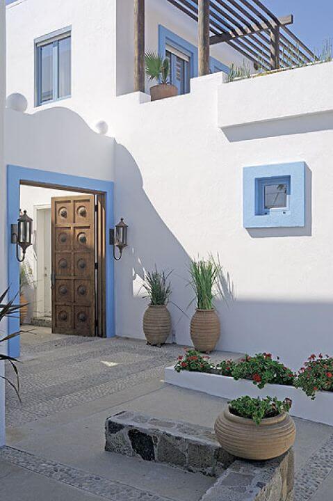 Drewniana brama ozdobiona elementami z kutego żelaza prowadzi na mały dziedziniec wyłożony betonem i kostką brukową.