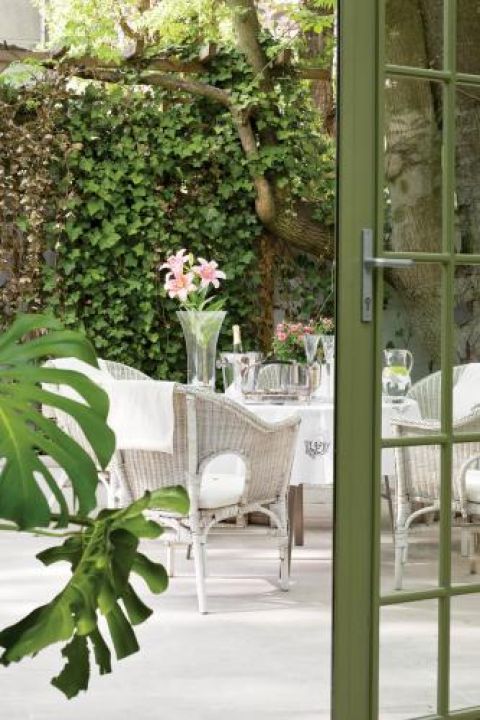 Jasna posadzka i białe meble ogrodowe pięknie komponują się z intensywną zielenią.