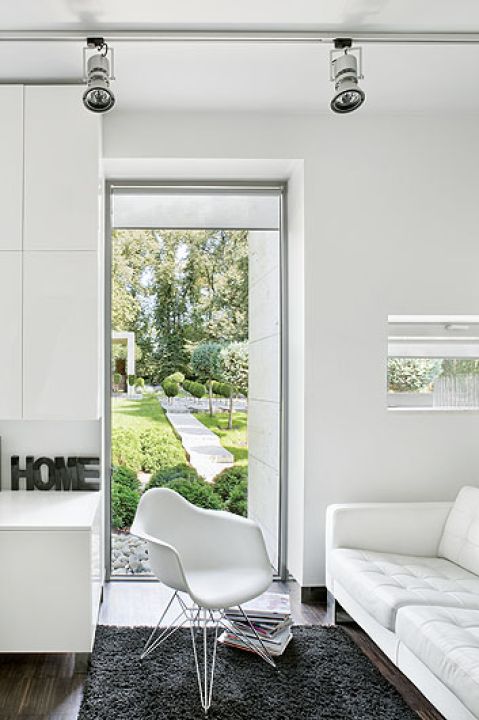 Skórzana kanapa i widok na ogród. A tam trawertynowy chodnik, kule z tui wśród białych kamieni i przystrzyżone cisy.