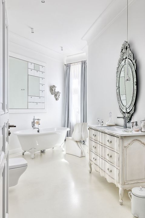 W łazience mieszają się elementy stylowe z dizajnerskimi: obok wanny na ozdobnych nóżkach przezroczysty stołek