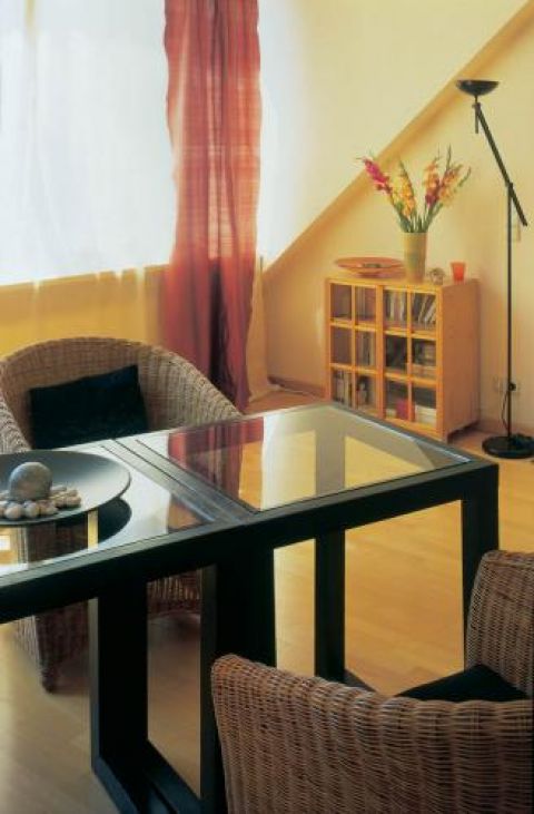 Plecione fotele, stół ze szklanym blatem i niska biblioteczka,