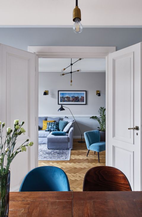 PRZY STOLE KRZESŁA – FAMEG, LAMPA WISZĄCA MOLECULAR – HOUSE DOCTOR Z N S HOME. NAD KANAPĄ PEJZAŻ PRZEDWOJENNEJ WARSZAWY,