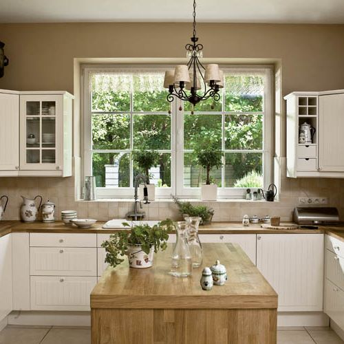 Do kuchni w podmiejskim domu pasują proste białe meble z drewnianymi blatami.