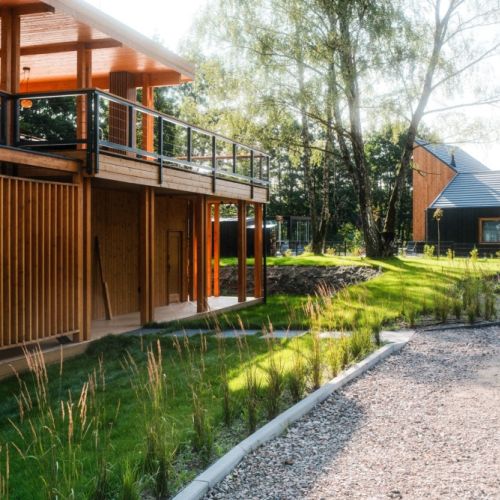 Naturalny ogród wokół domu w Kalborni na Mazurach Zachodnich. Drewniany taras i brak wyznaczonych granic działki płynnie łączą architekturę z lasem.