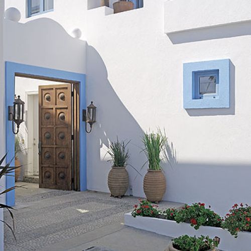 Drewniana brama ozdobiona elementami z kutego żelaza prowadzi na mały dziedziniec wyłożony betonem i kostką brukową.