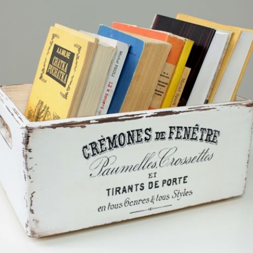 Drewniana skrzynka pomalowana na biało, przecierana na krawędziach w celu postarzenia. Dłuższe boki skrzynki ozdobione