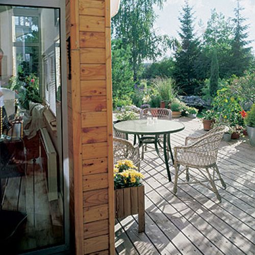 Drewniany taras otacza ogród pełen drzew i kwiatów.