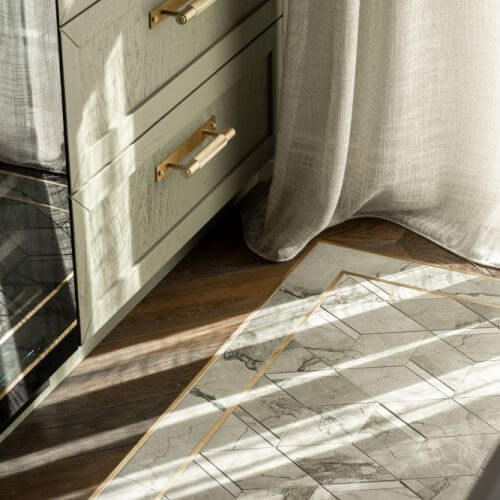 elegancki chodnik z płytek ułożony na drewnianej podłodze w pobliżu szafki kuchennej w odcieniu szałwiowej zieleni