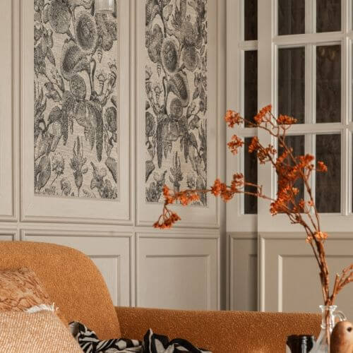 elegancki salon z musztardową sofą i sztukaterią ścienną, w którą wkomponowano czarno-białe tapety z motywem kwiatowym