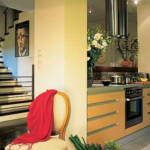 Geometryczne formy schodow i kuchennych szafek ocieplają kolorowe dodatki.