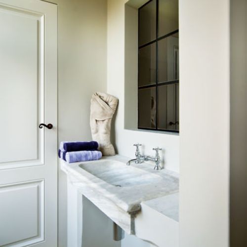 Kamienna umywalka obok chromowanej baterii, zabawne okucia, tkaniny i trochę sztuki.