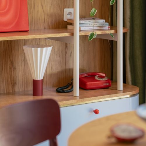 zaokrąglona biblioteczka z biało-bordową lampą stołową o plisowanym kloszu