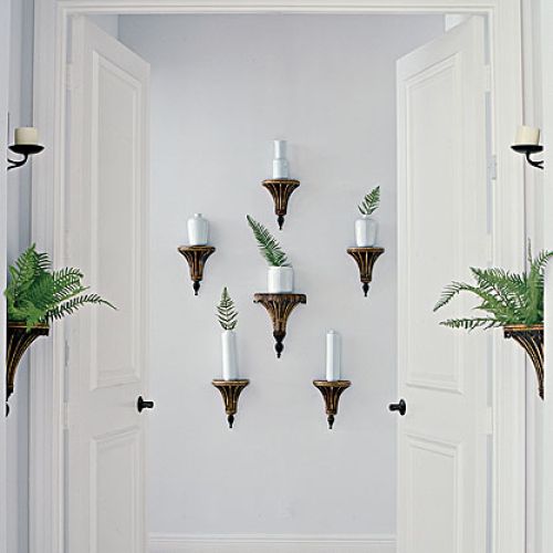 Kompozycja ze starych kinkietów, tyle tylko że zamiast żarówek projektant dodał im białe wazoniki i powkładał w nie liście