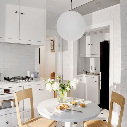 Kuchnia urządzona na biało - piękne kafle na ścianie i płytki na podłodze - w charakterystycznym dla międzywojnia kształcie i rozmiarze.