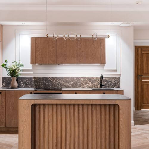 Otwarta kuchnia z zaokrągloną wyspą w stylu warm minimalism. Meble na wymiar wykończone naturalnym fornirem i ciemnym kamieniem.