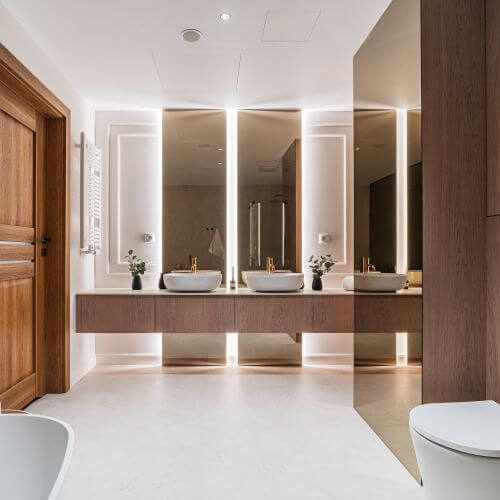 Duży salon kąpielowy z podwójną strefą umywalkową i imponującymi lustrami. Szlachetne materiały wykończeniowe i ciepłe, nastrojowe oświetlenie.