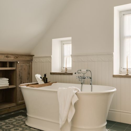 Pokój kąpielowy z wolnostojącą wanną. Dekoracyjna ceramiczna boazeria i klasyczne baterie nadają wnętrzu ponadczasową elegancję.
