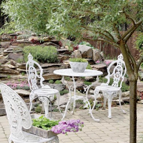 Miejsce do wypoczynku obok sadzawki z wodospadem. Metalowy stolik i krzesła w stylu rustykalnym podkreślają