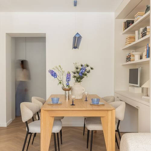 Drewniany stół, beżowe krzesła i niebieska lampa nad stołem w jadalni w mieszkaniu 60 m2 w bloku