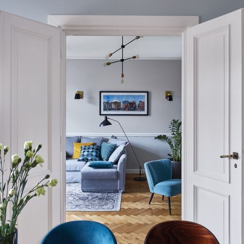 PRZY STOLE KRZESŁA – FAMEG, LAMPA WISZĄCA MOLECULAR – HOUSE DOCTOR Z N S HOME. NAD KANAPĄ PEJZAŻ PRZEDWOJENNEJ WARSZAWY,