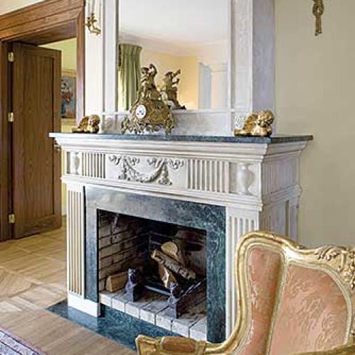 Na kominku stoją złocone dekoracje. Rezydencja strojna w antyki