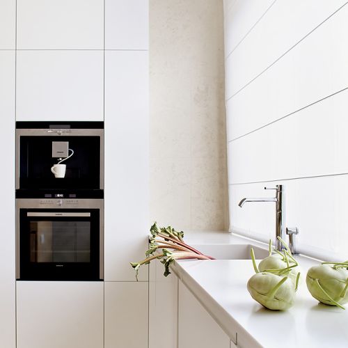 Na podłodze leży wapień perlino bianco. Matowe szafki zestawiono z wyspą-stołem z szarzonego dębu. Sprzęt