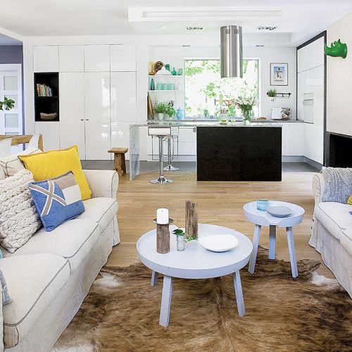 Nad stołem z mazurskich desek wiszą dizajnerska lampa LZF i obraz katarzyny Szymańskiej. Stoliki, pufy w kolorze ochry, szary