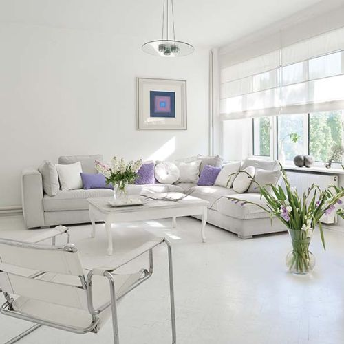 Salon z wielkimi oknami i piecem kaflowym. Fioletowe akcenty przełamują biel.