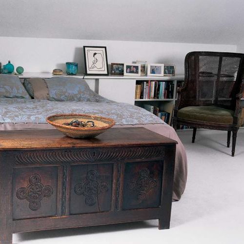 Przy łóżku stoi skrzynia zdobiona ornamentami roślinnymi.