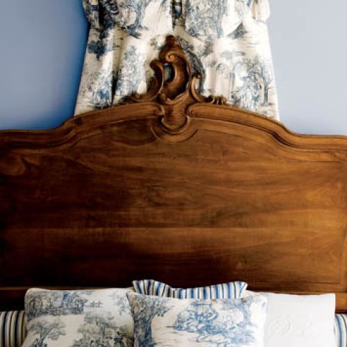 Rzeźbione wezgłowie zabytkowego łóżka, nad nim minibadachim z toile de jouy.
