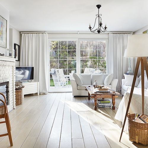 Salon w bieli. Zamiast marmuru wokół kominka cegła i drewniane decha pomalowana na biało.