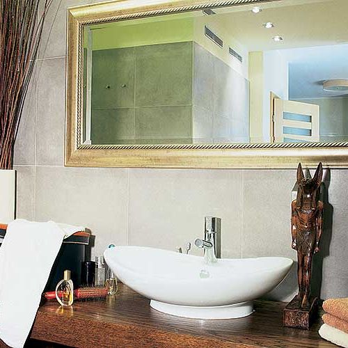 Solidny drewniany blat, ozdobna umywalka i złocona rama lustra kontrastują z surowością przypominającego beton gresu.