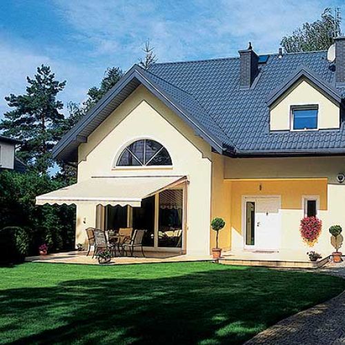 Szmaragdowe tuje okalają działkę gęstym szpalerem, pośrodku jest zadbany trawnik.