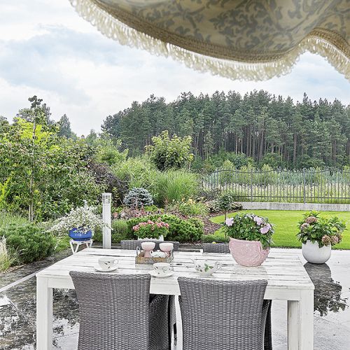 Urządzony naturalnie, sielsko: stół, plecione fotele, kwiaty.