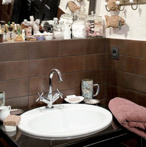 W łazience świetnie sprawdza się połączenie piaskowej ściany z brązowymi płytkami.