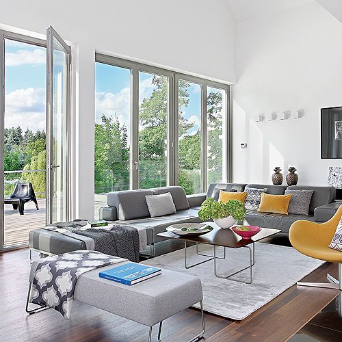 W salonbie dominują szarości (kanapy) rozweselone kolorowymi fotelami i dodatkami, np. poduszkami i pledami.