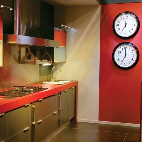 Zegar w kuchni jest niezbędny, ale dwa to już ekstrawagancja. Podobnie jak czerwona ściana i dobrany pod kolor blat